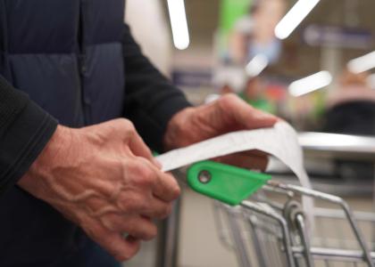 The hands of an older man holding a receipt over a shopping cart in a store