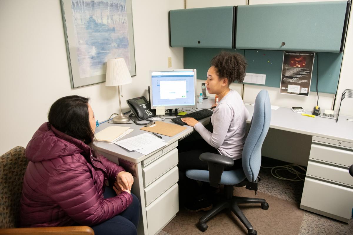 Student seated in front of computer monitor discussing files with patient.